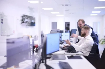 Sales Manager coaching a colleague at computer in modern office environment